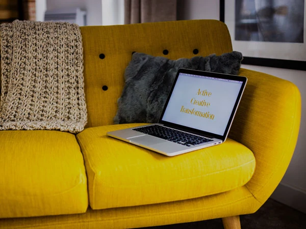 Laptop on the couch with the words "Active Creative Transformation" written on the screen